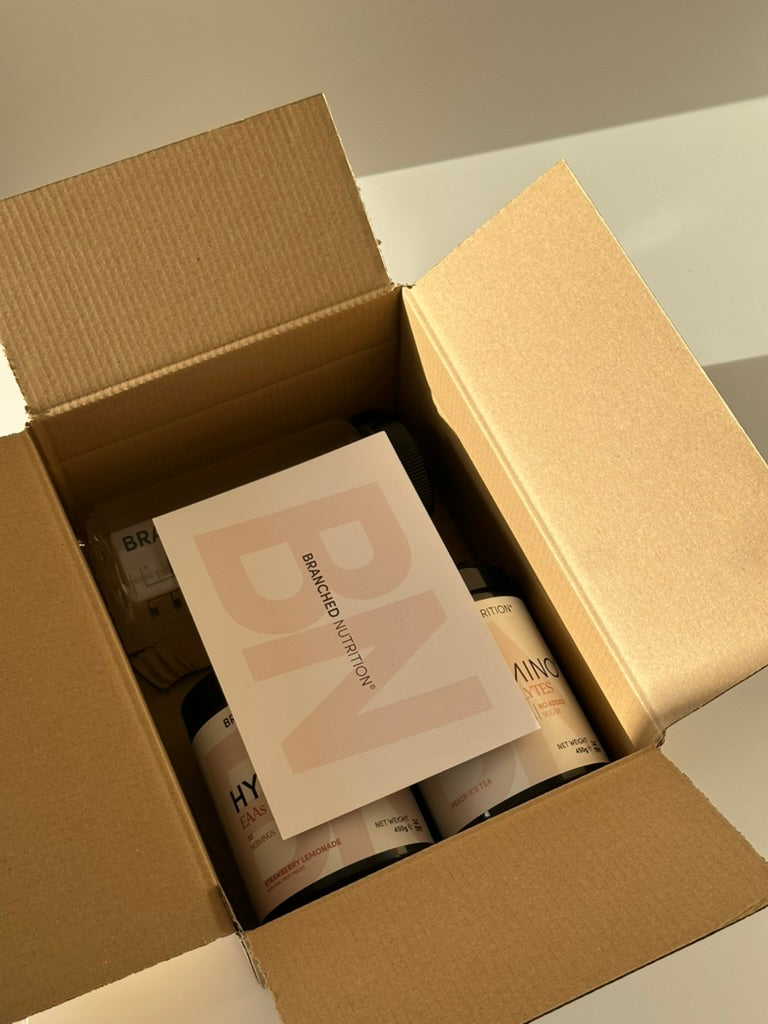 An open Branched Nutrition delivery box with HYDRAMINO tubs and a branded card
